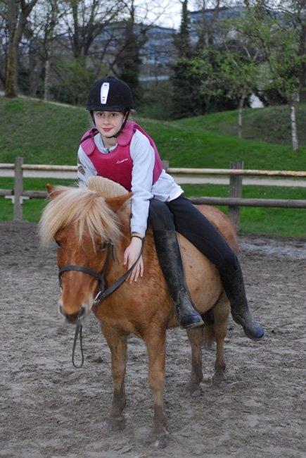 Enfant sur le dos d'un poney Shetland alezan portant un gilet d'équitation rose ajusté pour sa sécurité